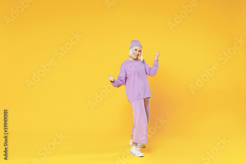 Full length of young blonde caucasian woman 20s bob haircut in casual basic purple suit beanie hat doing winner gesture clenching fists saying yes isolated on yellow background studio portrait.