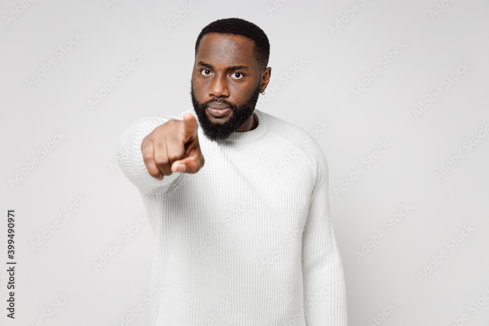 Displeased dissatisfied strict angry young african american man 20s wearing casual basic sweater standing pointing index finger on camera isolated on white color wall background studio portrait. Displeased dissatisfied strict angry young african american man 20s wearing casual basic sweater standing pointing index finger on camera isolated on white color wall background studio portrait.