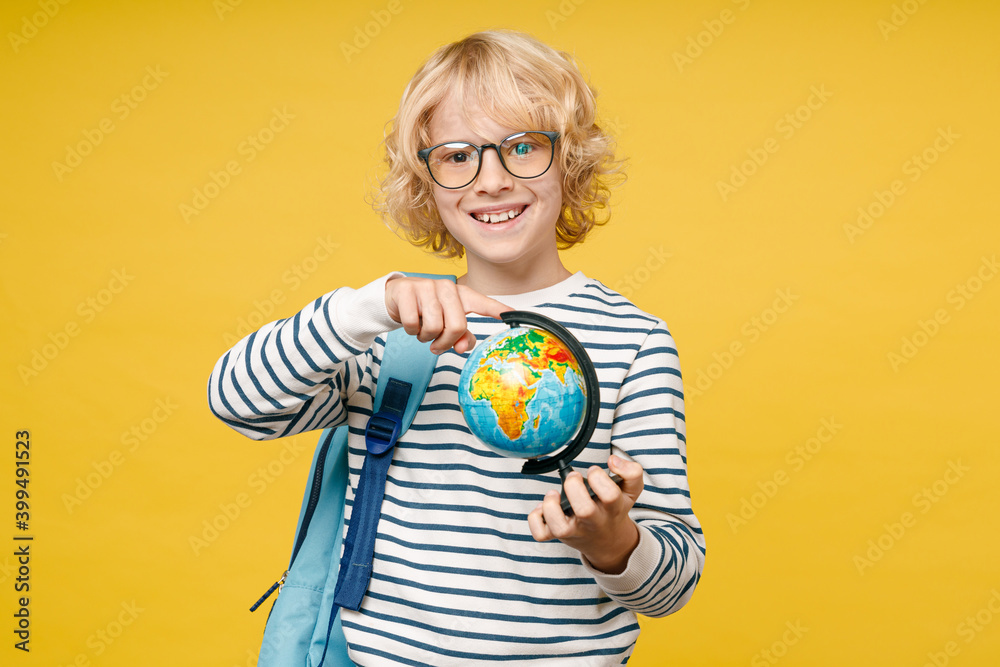 Smiling male kid teen boy 10s years old in striped sweatshirt glasses backpack point index finger on world Earth globe isolated on yellow color background, child studio portrait. Education concept. Smiling male kid teen boy 10s years old in striped sweatshirt glasses backpack point index finger on world Earth globe isolated on yellow color background, child studio portrait. Education concept.