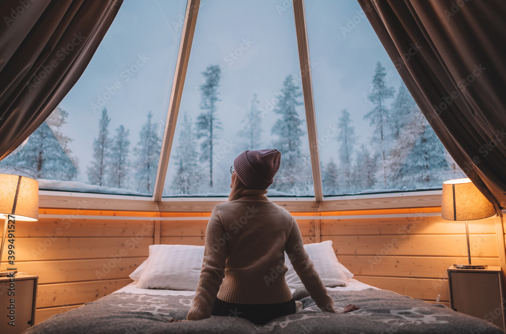 woman sitting on the bed in aurora cabin in Finland observing the nature and landscape 
