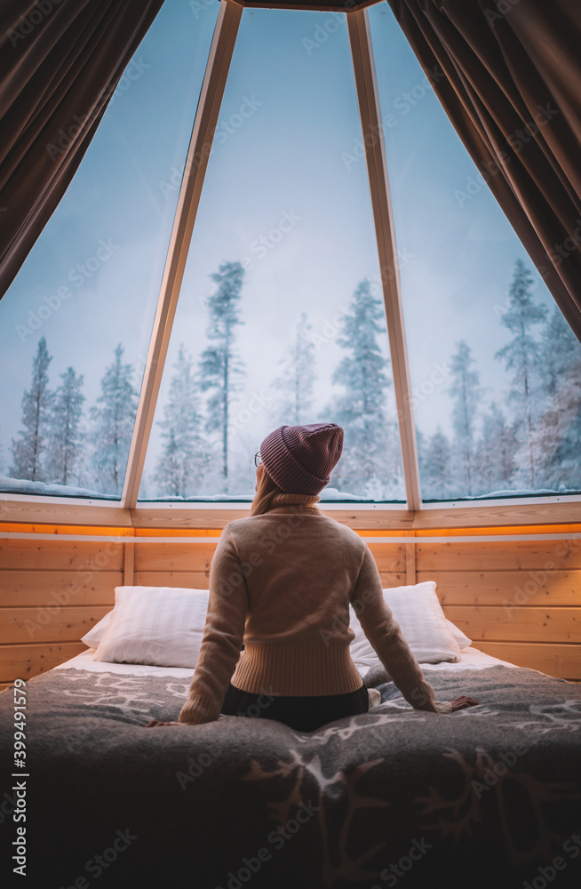 woman sitting and observing the nature on the bed in the aurora cabin in Finland 