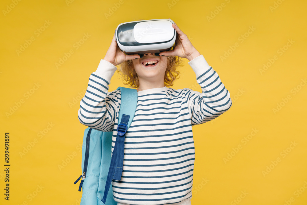 Cheerful little male kid teen boy 10s years old wearing striped sweatshirt glasses backpack watching in vr headset gadget isolated on yellow color background, child studio portrait. Education concept. Cheerful little male kid teen boy 10s years old wearing striped sweatshirt glasses backpack watching in vr headset gadget isolated on yellow color background, child studio portrait. Education concept.