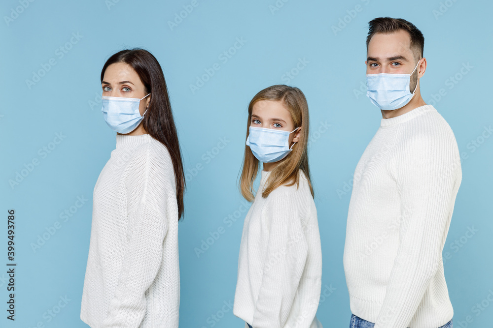 Side view of young parents mom dad with child kid daughter teen girl in sweaters sterile face mask safe from coronavirus virus covid-19 isolated on blue background. Family day parenthood concept.
