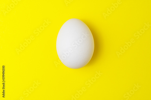 One white chicken egg on yellow background with empty space.
