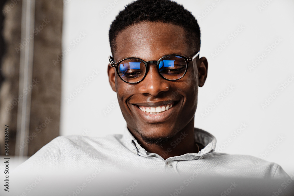 Afro american man in eyeglasses smiling and working with laptop indoors Afro american man in eyeglasses smiling and working with laptop indoors