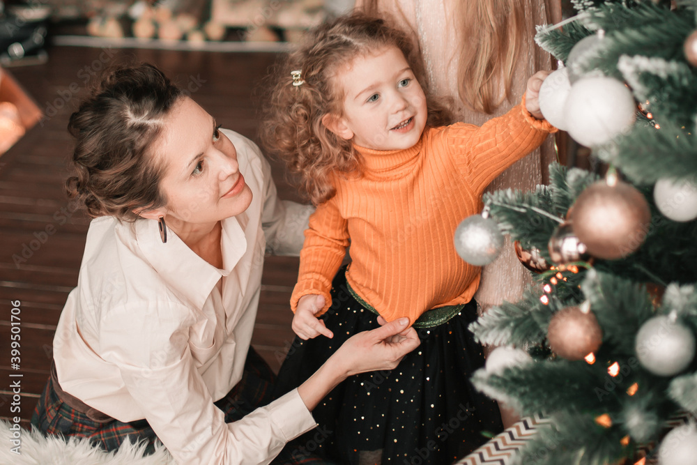 mom and her little daughters decorating the Christmas tree mom and her little daughters decorating the Christmas tree