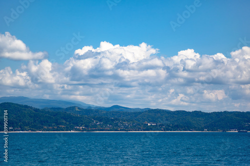 Sea and mountains against the blue sky with white clouds, at the bottom of the mountains are buildings