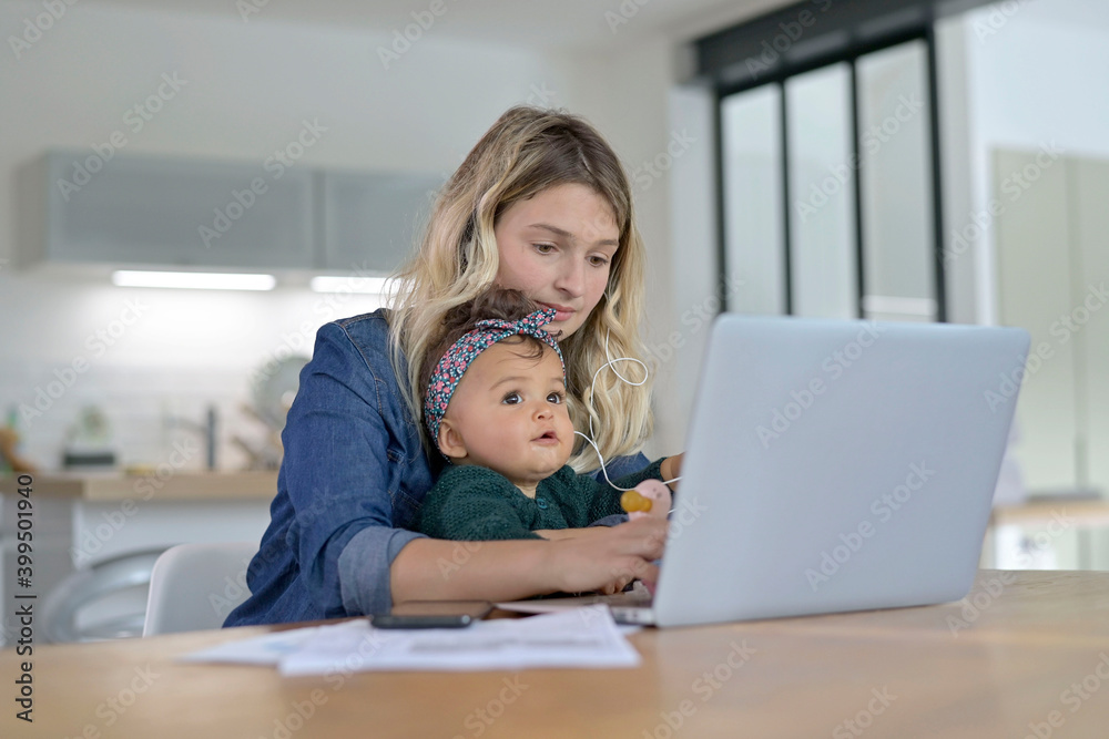 Young woman teleworking from home and watching baby girl Young woman teleworking from home and watching baby girl