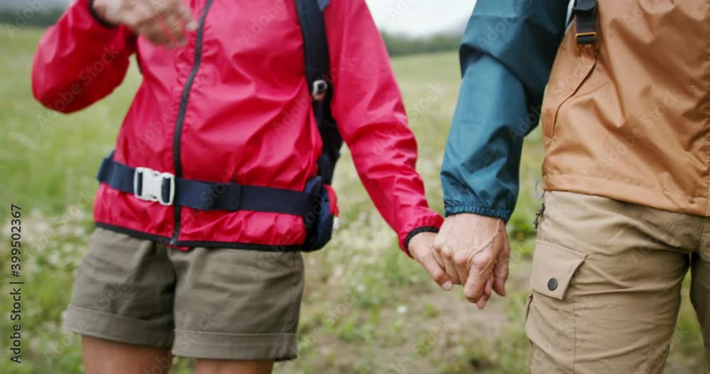 Senior pensioner couple hikers walking in nature, holding hands.