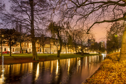 Rotterdam, The Netherlands, December 13, 2020: trees, fallen leaves and the reflection of lighttrails and historic houses in the water of Noordsingel canal in the blue hour