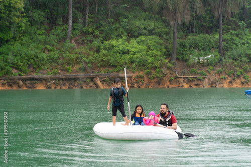 Family wearing life jackets paddling on an inflatable boat in Kenyir Lake, Malaysia.