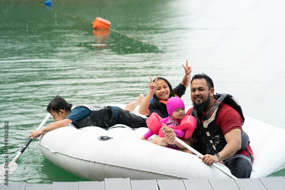 Naklejka premium Family wearing life jackets paddling on an inflatable boat in Kenyir Lake, Malaysia.