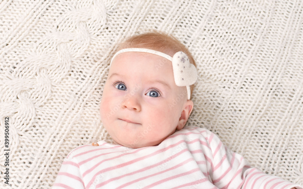 Cutest little 4- 5 months old caucasian baby girl with bow-heart in striped T-shirt on white plaid. Valentine day concept. Look at camera. Cutest little 4- 5 months old caucasian baby girl with bow-heart in striped T-shirt on white plaid. Valentine day concept. Look at camera.