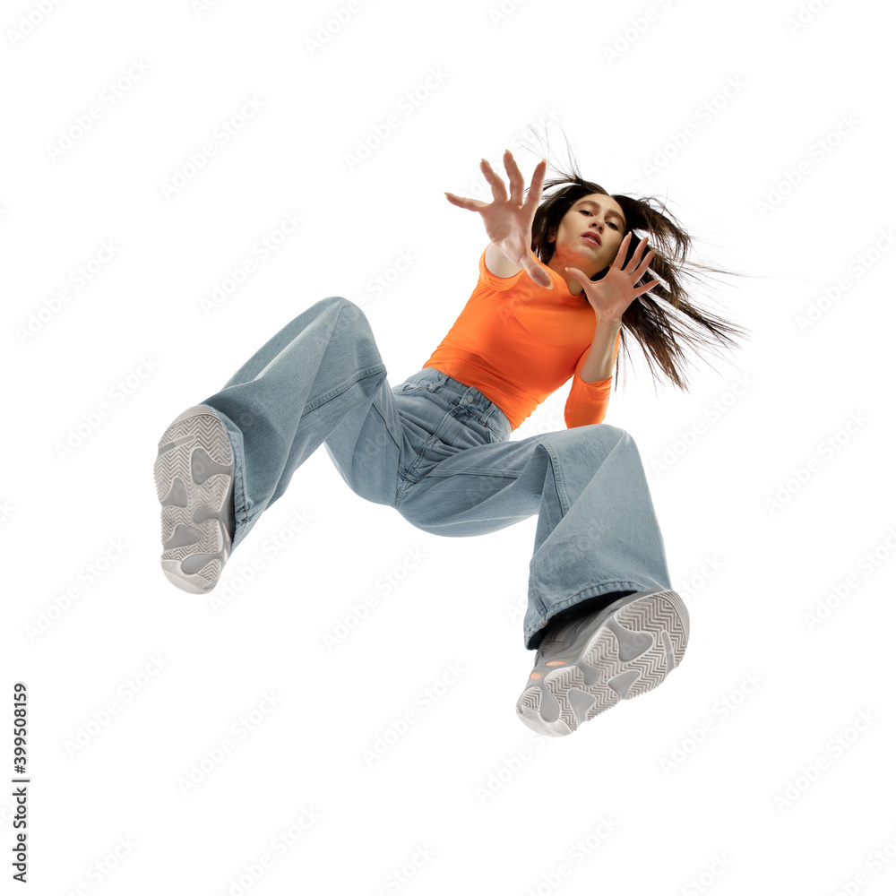 Dancing. Young stylish woman in modern street style outfit isolated on white background, shot from the bottom. West fashionable model in sneakers and sweetshirt, musician, rapper performing. - obrazy, fototapety, plakaty 