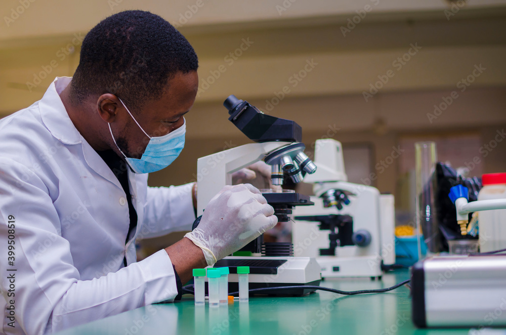 young handsome african scientist in the lab carefully carrying out experiments while using a microscope young handsome african scientist in the lab carefully carrying out experiments while using a microscope