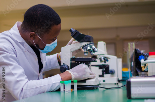 young handsome african scientist in the lab carefully carrying out experiments while using a microscope