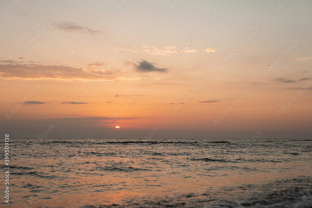 Colorful sunset on a sandy beach, waves with foam on the sand. Ocean, coast. Soft selective focus.