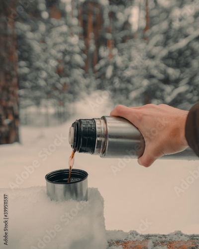 Pouring delicious tea into a thermos mug in a snowy forest