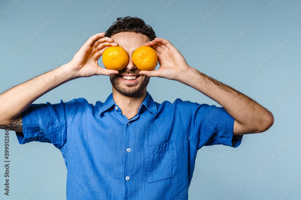 Joyful handsome guy smiling while making fun with mandarins Joyful handsome guy smiling while making fun with mandarins