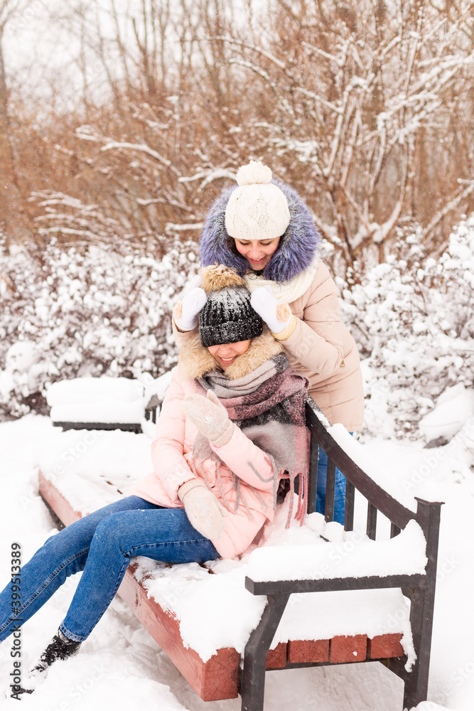 Obraz premium Two girls are walking in a winter park in the snow. Sisters on the background of snowy trees