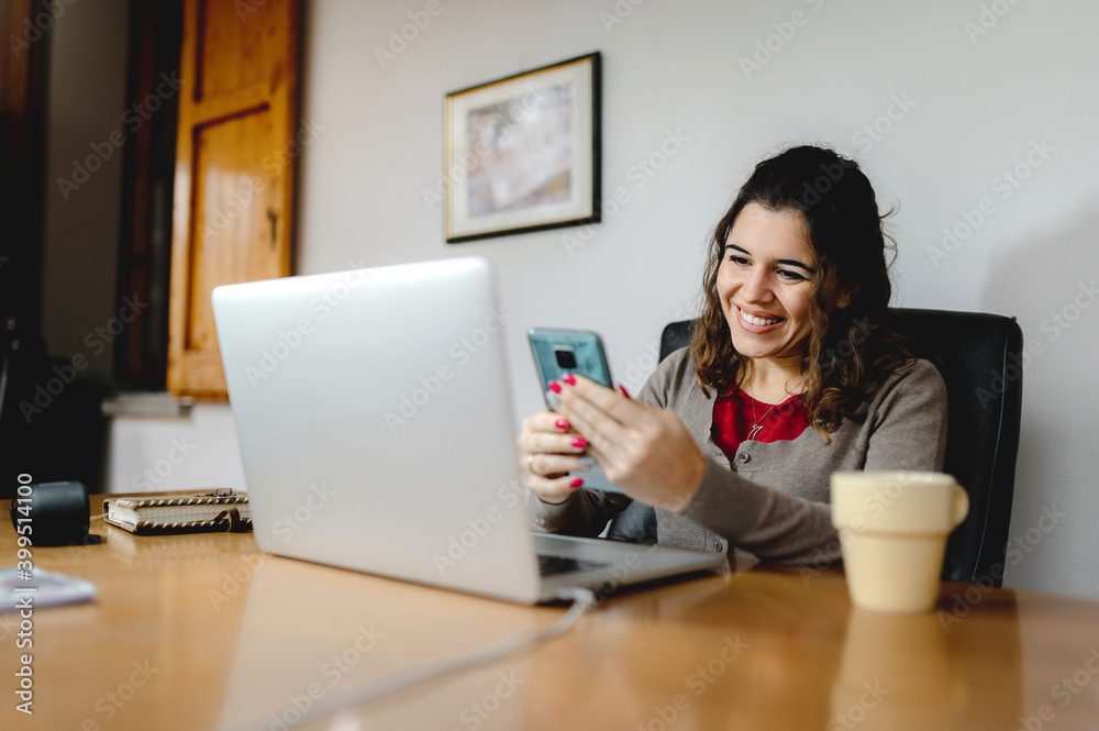 Close-up frontal portrait young smiling attractive woman working at office desk with computer laptop using smartphone. Close-up frontal portrait young smiling attractive woman working at office desk with computer laptop using smartphone.