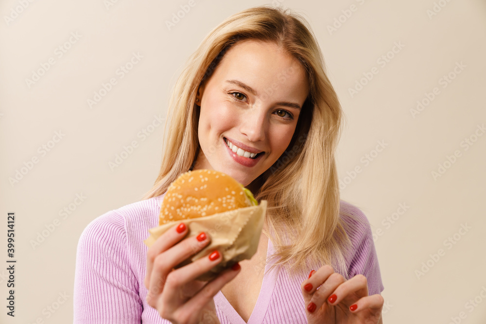 Cheerful beautiful girl smiling while showing hamburger at camera