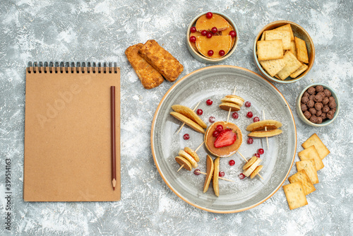 Pancake decoration with fruits and biscuits next to notebook on white background