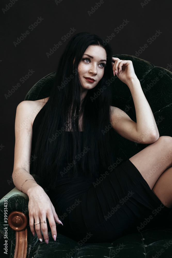 Slender brunette is sitting in dress on the couch. New Year's Eve, dark background. Slender brunette is sitting in dress on the couch. New Year's Eve, dark background.