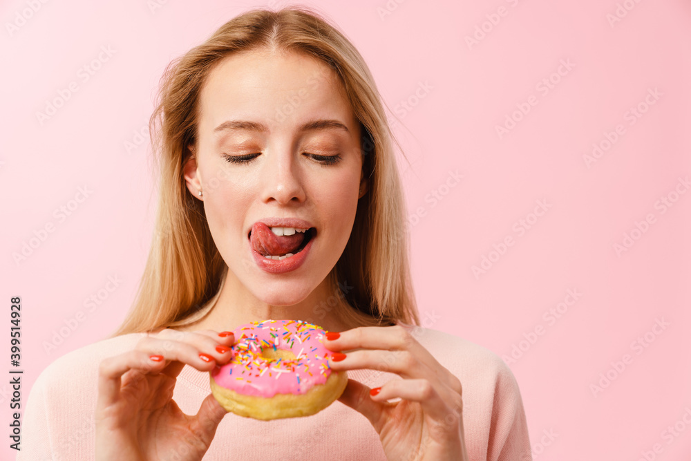 Pleased charming blonde girl showing her tongue while eating doughnut