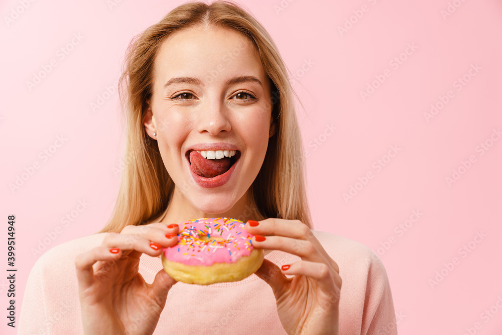 Joyful charming blonde girl showing her tongue while eating doughnut