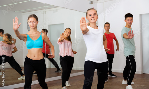 Group of teenagers participating in dance class  following their young female teacher in dance school