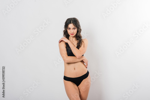 Cute brunette female model posing, wearing black and red underwear in white studio