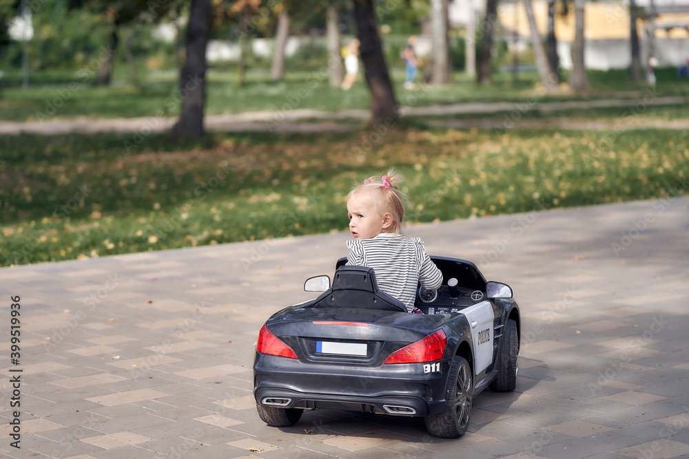 A little girl is riding a children's toy car without looking ahead. back view.