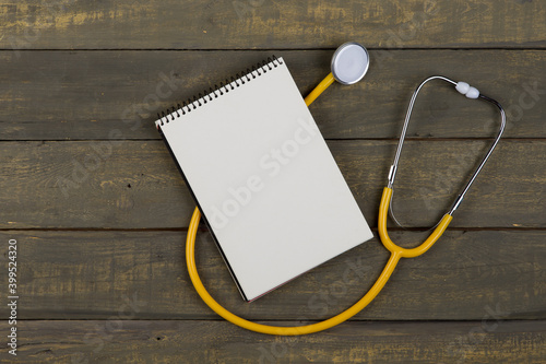 Medical and health care concept - yellow stethoscope and blank spiral notepad on wooden background