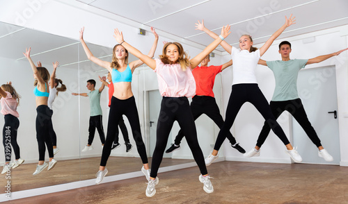 Group of sportive teenagers with female teacher training in modern dance hall, jumping together