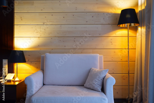 Beige armchair and lamps, wooden wall background. Comfort, interior, cosiness concept. Front view, copy space