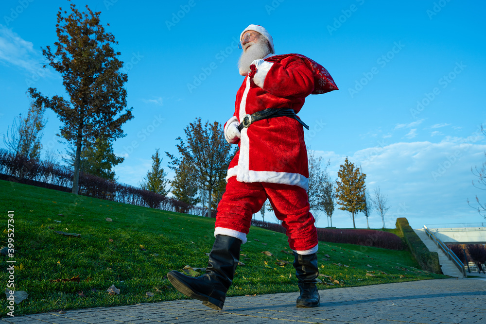 Obraz premium funny Santa Claus walking down the street with a bag of gifts