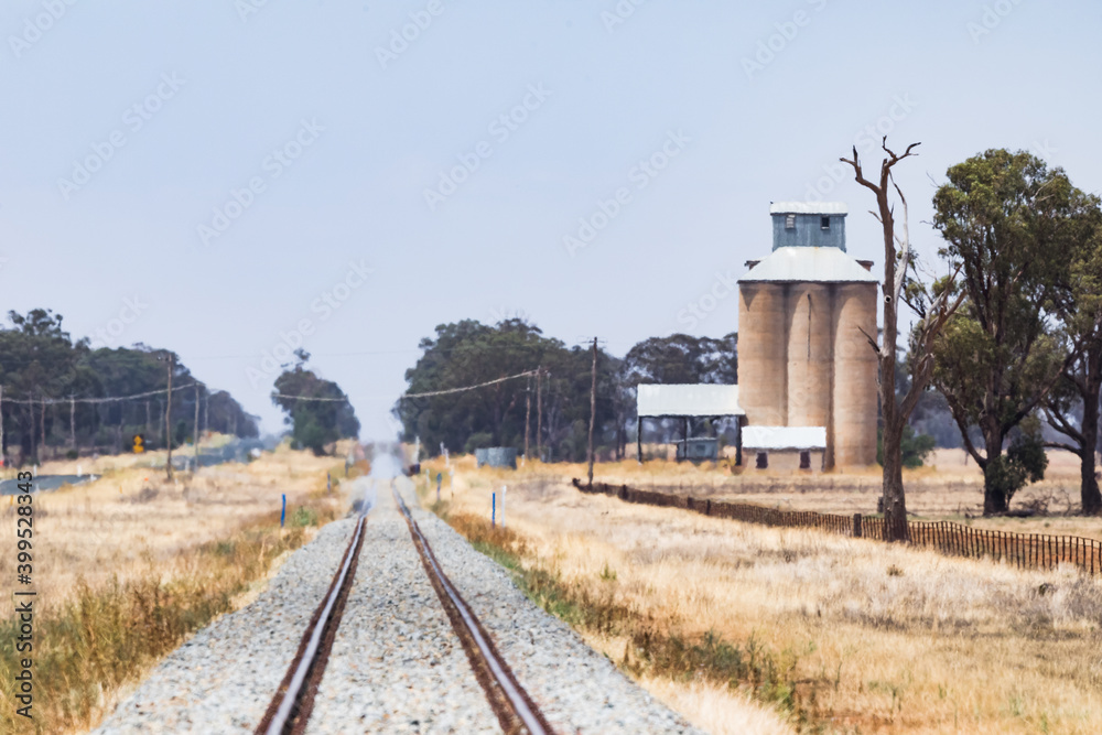 Heat haze during drought conditions along straight rail tracks in Outback Australia with grain storage silo. Copy space.