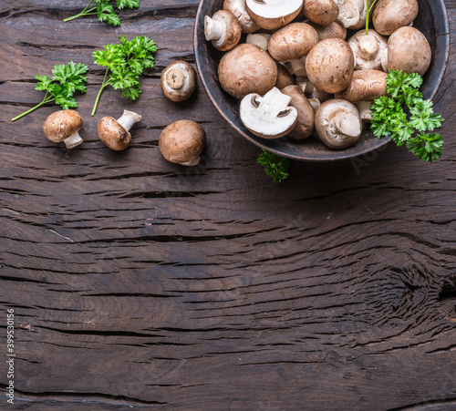 Brown colored common mushrooms on wooden table with herbs. Top view.