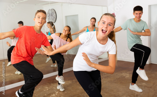 Teenage girl dancer practicing active vigorous dance with group in modern studio..