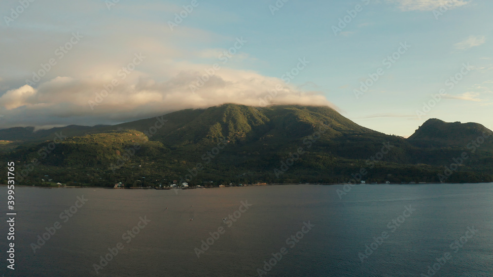 Coastline of tropical island covered with green forest against the blue sky with clouds at sunset, aerial view. Seascape: Ocean and sky.Philippines, Camiguin.