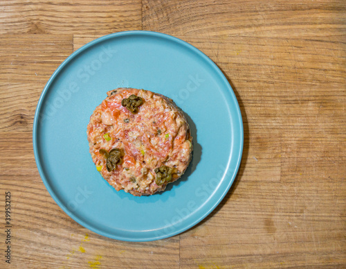 Salmon tartare with capers on plate on a wooden surface, top view