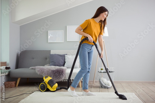 Beautiful young girl in a good mood makes house cleaning with a vacuum cleaner photo