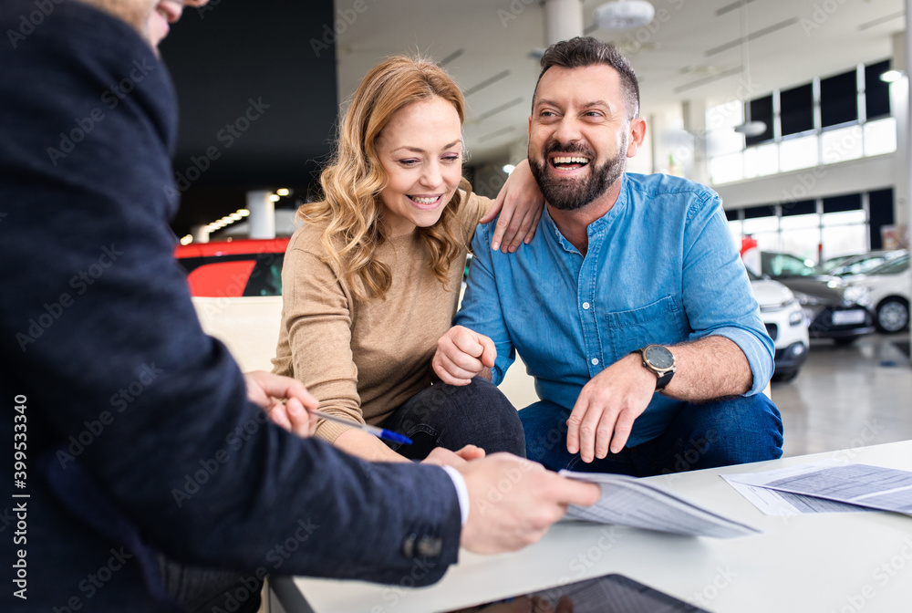 Mid-adult couple talking with sales agent and signing contract for new car in modern car showroom. Mid-adult couple talking with sales agent and signing contract for new car in modern car showroom.