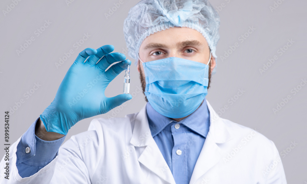 Vaccination and health protection. Male doctor in facial mask holding vaccine or medication on grey background Vaccination and health protection. Male doctor in facial mask holding vaccine or medication on grey background