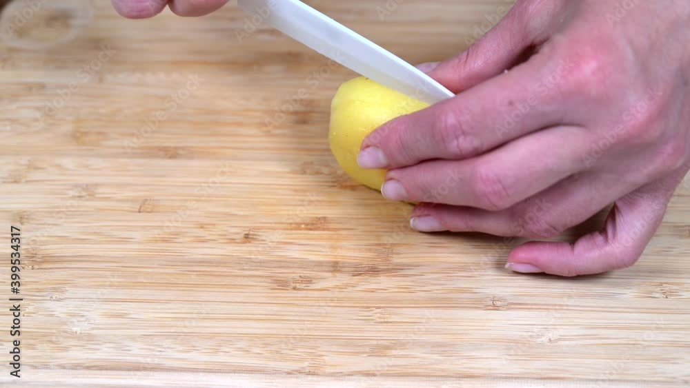 Female hand cuts potato for russian olivier salad with a white ceramic knife on wooden cutting board, close up 4k Female hand cuts potato for russian olivier salad with a white ceramic knife on wooden cutting board, close up 4k