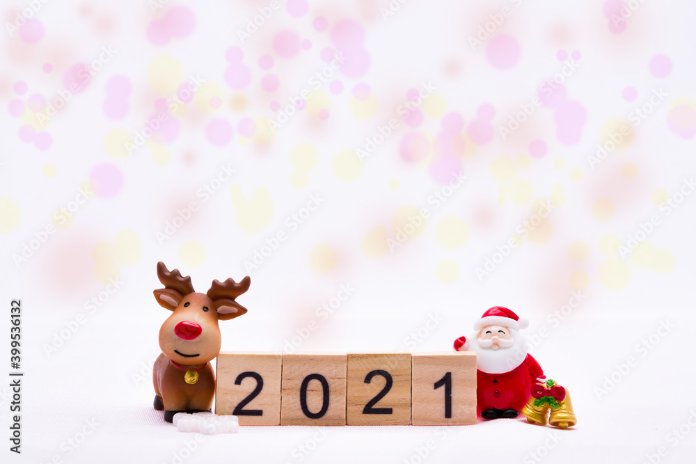 Naklejka premium Merry Christmas and Happy New Year 2021. Number 2021 on small wooden slats. Ceramic Santa Claus standing gold bell, brown Reindeer smiling. On white background and sweet bokeh.