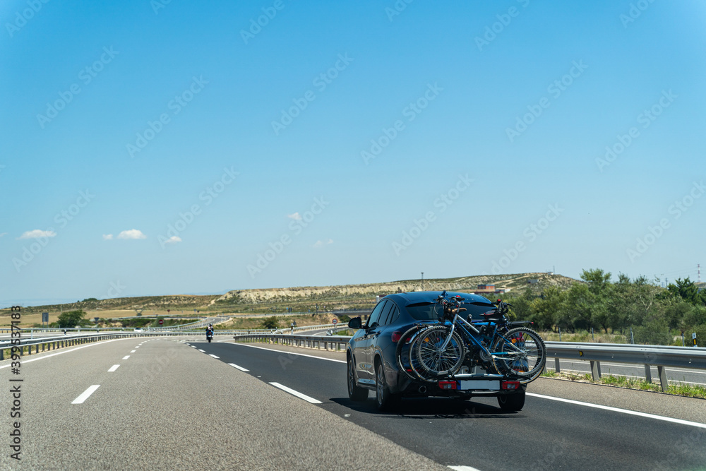 Car with two bicycles on desert road with blue sky and bushes on a summer day