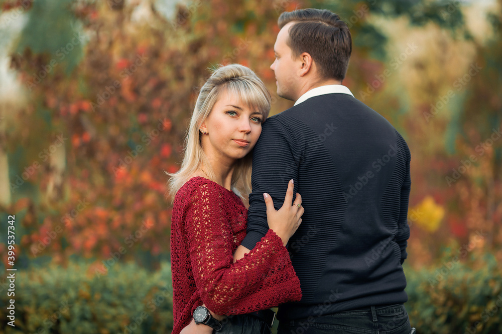 blonde girl in maroon sweater, brown-haired young man in blue sweater hug in the Park blonde girl in maroon sweater, brown-haired young man in blue sweater hug in the Park