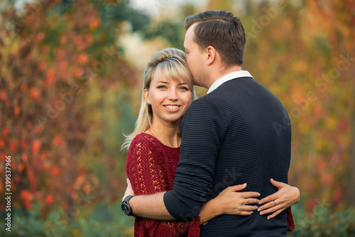 blonde girl in maroon sweater  brown-haired young man in blue sweater hug in the Park